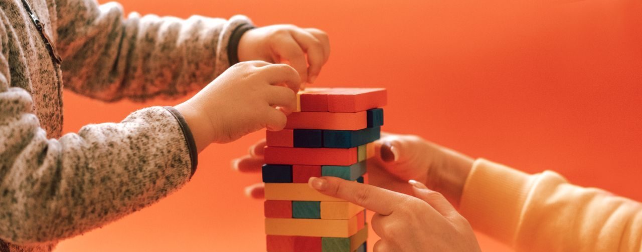 A child and adult play with colorful wooden blocks against an orange backdrop, emphasizing learning and creativity.